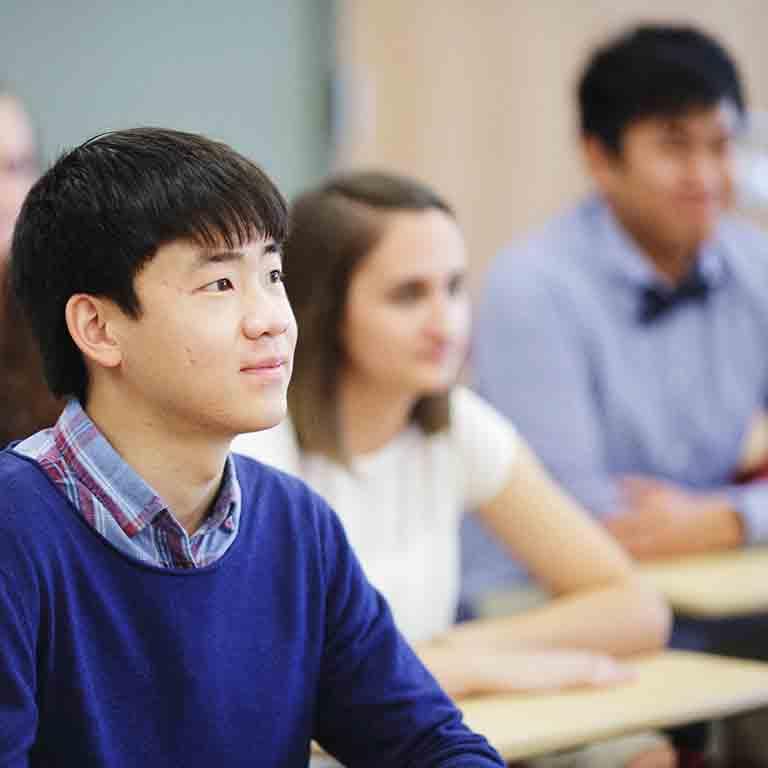 一个男学生坐在演讲厅里，聚精会神地望着前面.